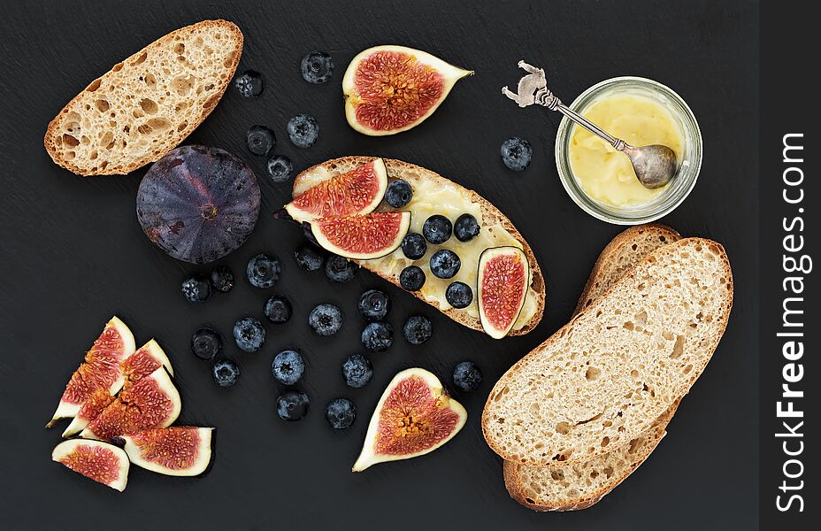 Fresh homemade bread, homemade baking. Blank for sandwich, figs, blueberries, sauce. Top view. Black stone background