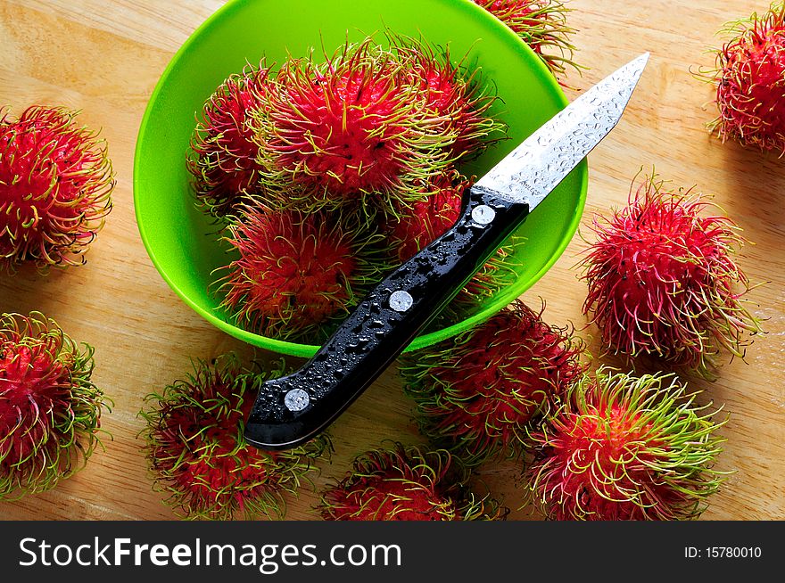 Fresh rambutans in green dish with knife as probs.