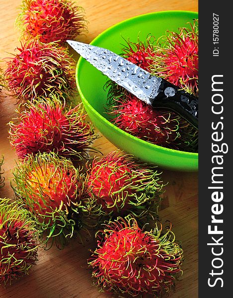 Fresh rambutans in green dish with knife as probs.