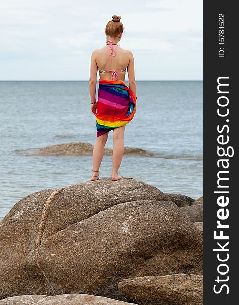 Woman on the beach, in bikini and bath towel with look to the sea