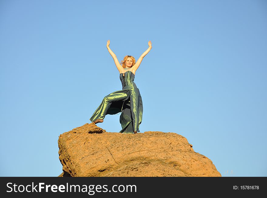 Attractive blond woman standing on a top of rock with arms outstretched. Attractive blond woman standing on a top of rock with arms outstretched