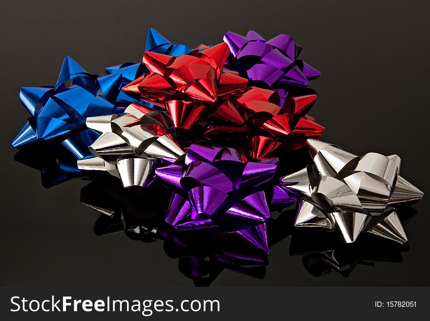 Many shiny silver red blue purple gift bows on black with reflection. Many shiny silver red blue purple gift bows on black with reflection