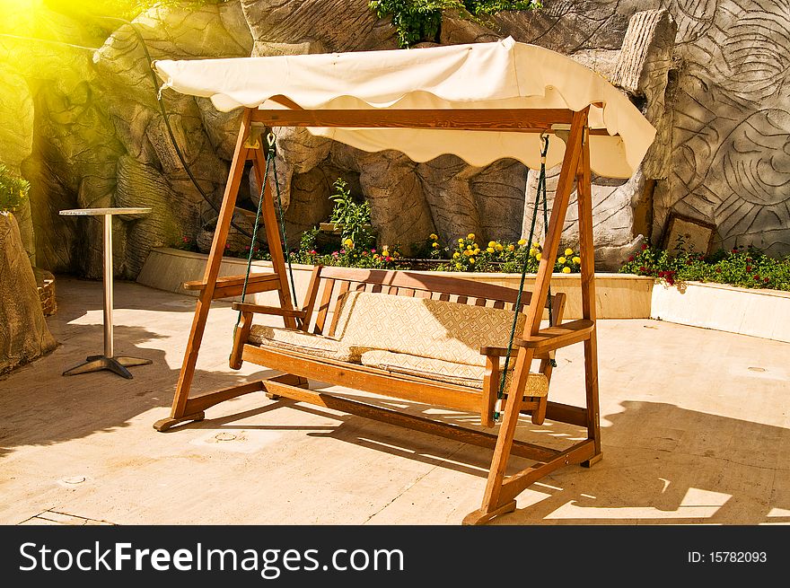 Abandoned splendid wooden swing next to the rock and flowers. Abandoned splendid wooden swing next to the rock and flowers.