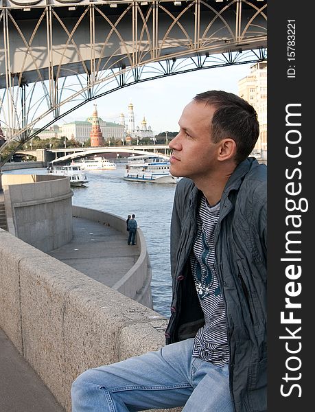 Attractive brunette young man sitting on the barrier near the Moscow river. Attractive brunette young man sitting on the barrier near the Moscow river