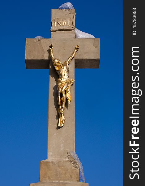 Golden statue of Jesus on a stone cross with a melting snow against a blue sky. Golden statue of Jesus on a stone cross with a melting snow against a blue sky.