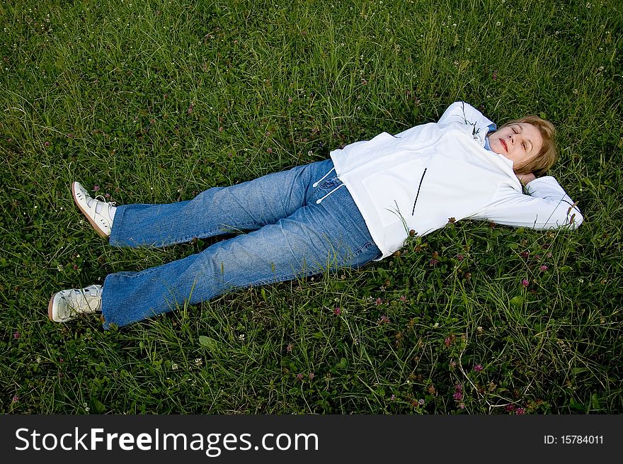 An elderly woman rests on flowering to the meadow.