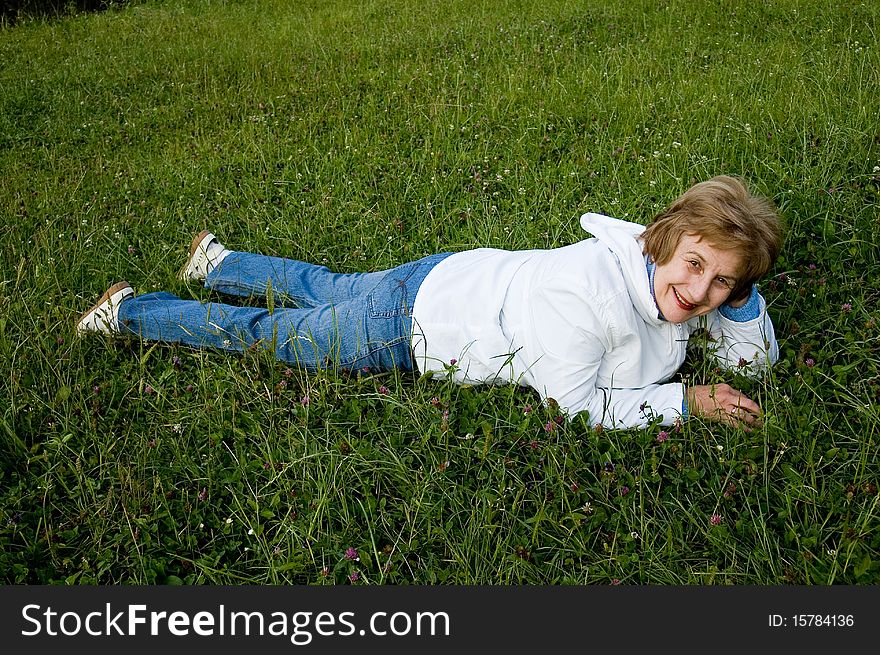 An elderly woman rests on flowering to the meadow. 
Smiles and looks in a photographic camera