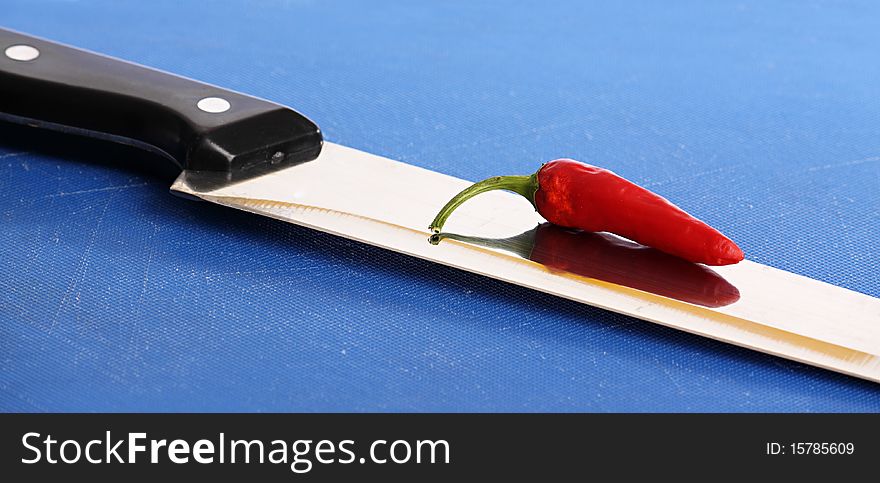 A red hot chili pepper on the blade of a kitchen knife. A red hot chili pepper on the blade of a kitchen knife