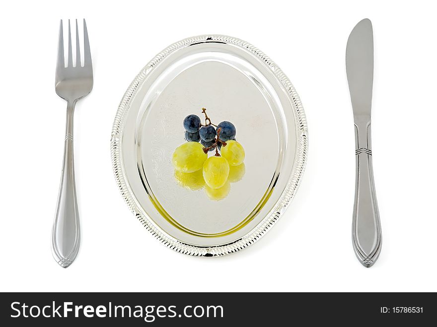 Some berries of a grape lay on a silver plate