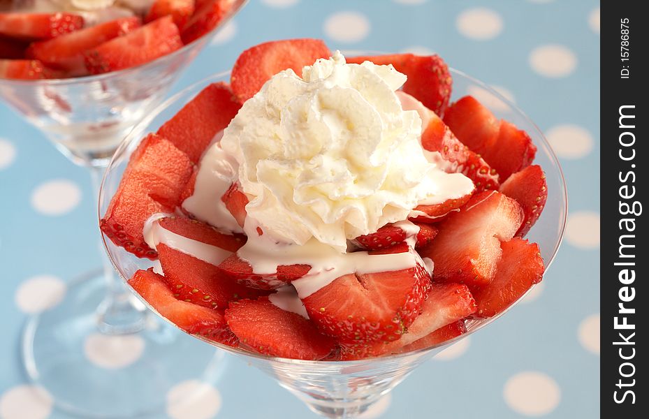 Sliced fresh strawberries with cream in martini glasses on blue polka dot background. Sliced fresh strawberries with cream in martini glasses on blue polka dot background