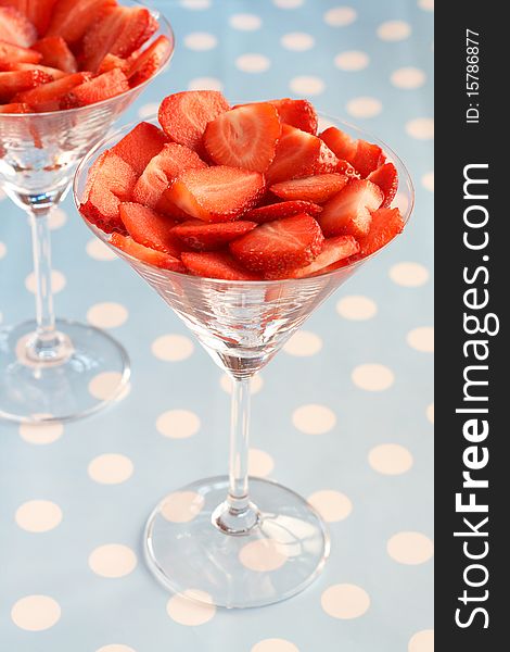 Sliced fresh strawberries in martini glasses on blue polka dot background. Sliced fresh strawberries in martini glasses on blue polka dot background