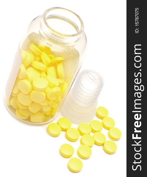 Glass bottle with yellow pills on white background
