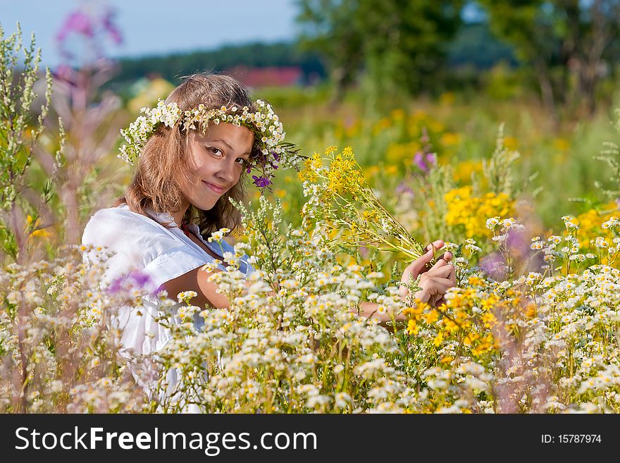 Russian girl in a wreath from camomiles is in a wheaten field