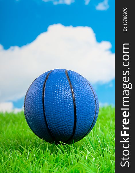 A blue basketball on a green lawn against a blue cloudy sky