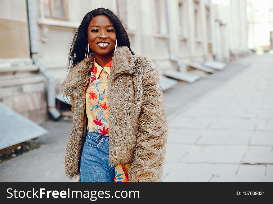 A beautiful and stylish black girl with long dark hair dressed in a brown coat and shirt wallking in a summer city. A beautiful and stylish black girl with long dark hair dressed in a brown coat and shirt wallking in a summer city