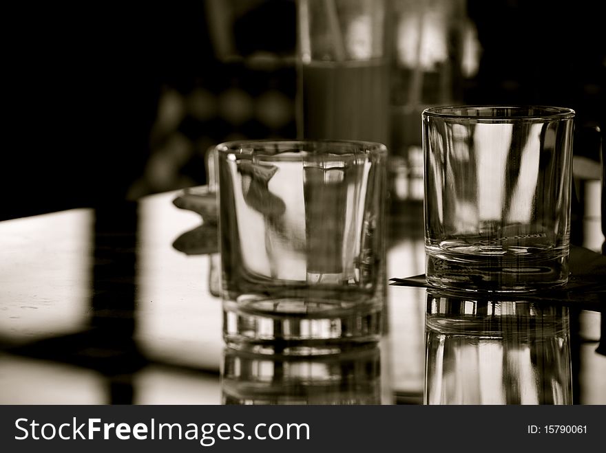 Some whisky glasses on a table and a glass for juice in the background. The reflection of the glasses and of the windowis visible in the background