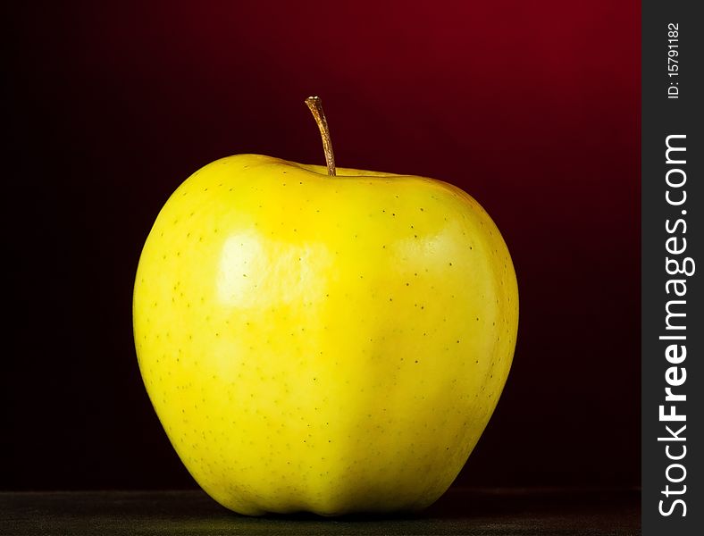 A Juicy yellow green apple with a red and black background