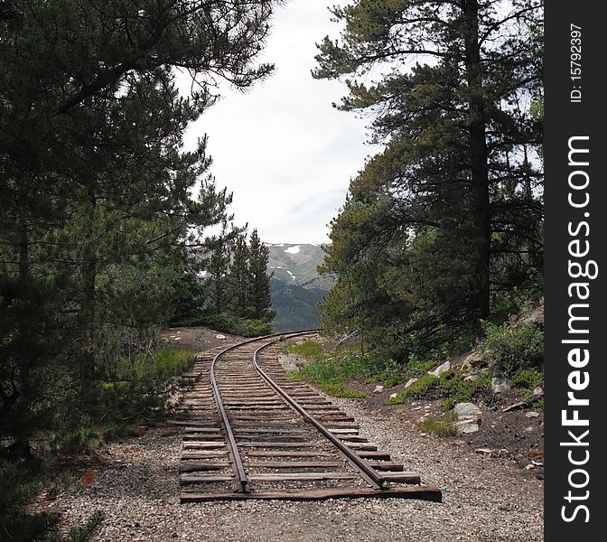 Old railroad tracks going around a bend with a view of the mountains ahead and trees beside it. Old railroad tracks going around a bend with a view of the mountains ahead and trees beside it.