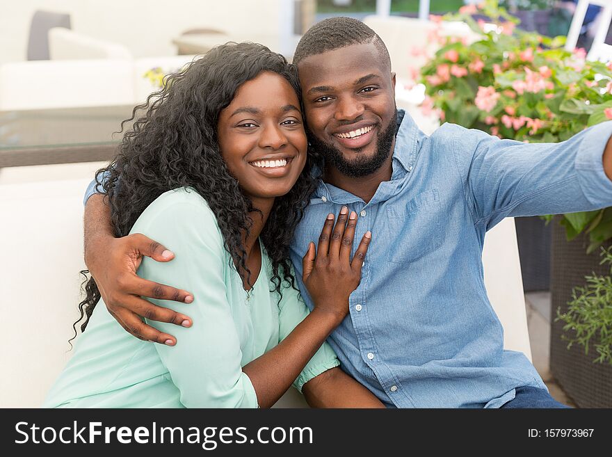 Young african couple hugging and sitting in cafe doing selfie