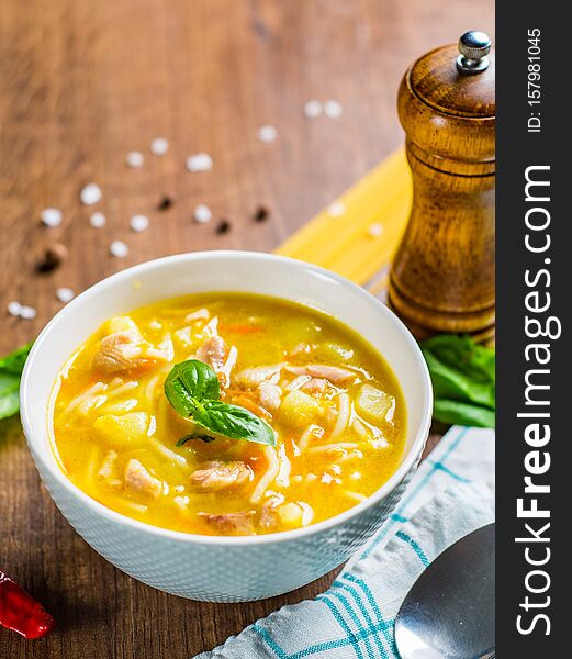 Chicken soup with noodles and vegetables in white bowl on wooden table
