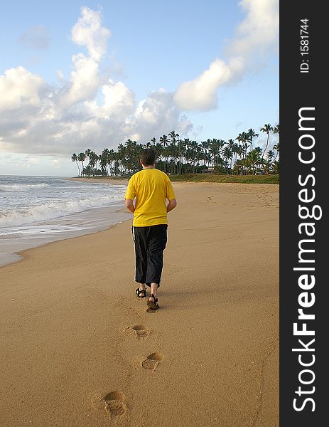 Man walking along an isolated carribean beach on a sunny morning with blue sky and palm trees in the distance with the waves lapping the shore. Man walking along an isolated carribean beach on a sunny morning with blue sky and palm trees in the distance with the waves lapping the shore