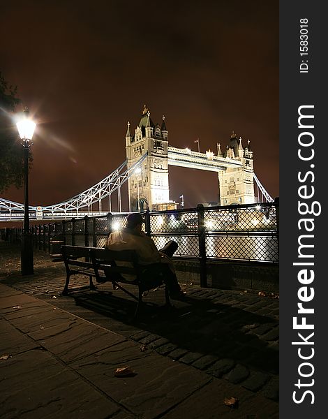 Man sitting on a bench in front of The Tower Bridge at night in London, UK. Man sitting on a bench in front of The Tower Bridge at night in London, UK