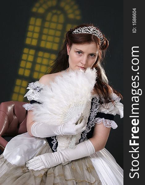 Girl in historic robe with fan in front of yellow window