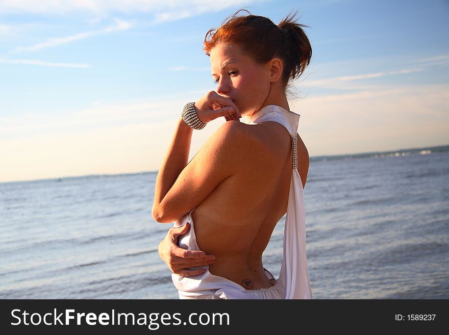 Young female dressed up, standing on a morning beach, thinking