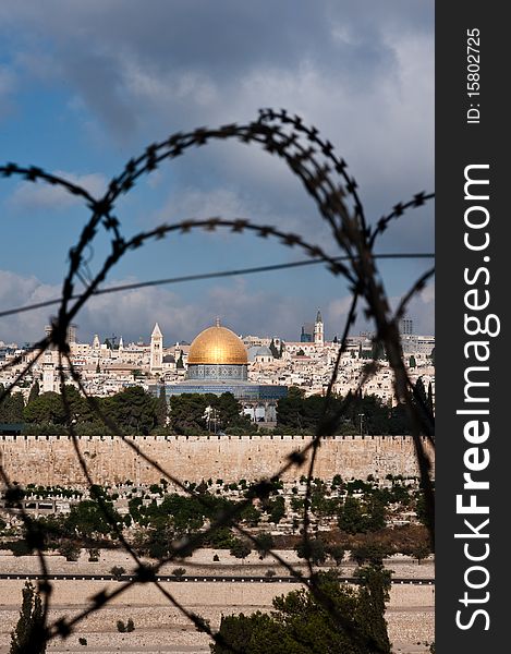 The Old City of Jerusalem, including the Dome of the Rock and various church steeples, seen through coils of razor wire, illustrating the Holy Land's history of division and conflict. The Old City of Jerusalem, including the Dome of the Rock and various church steeples, seen through coils of razor wire, illustrating the Holy Land's history of division and conflict.