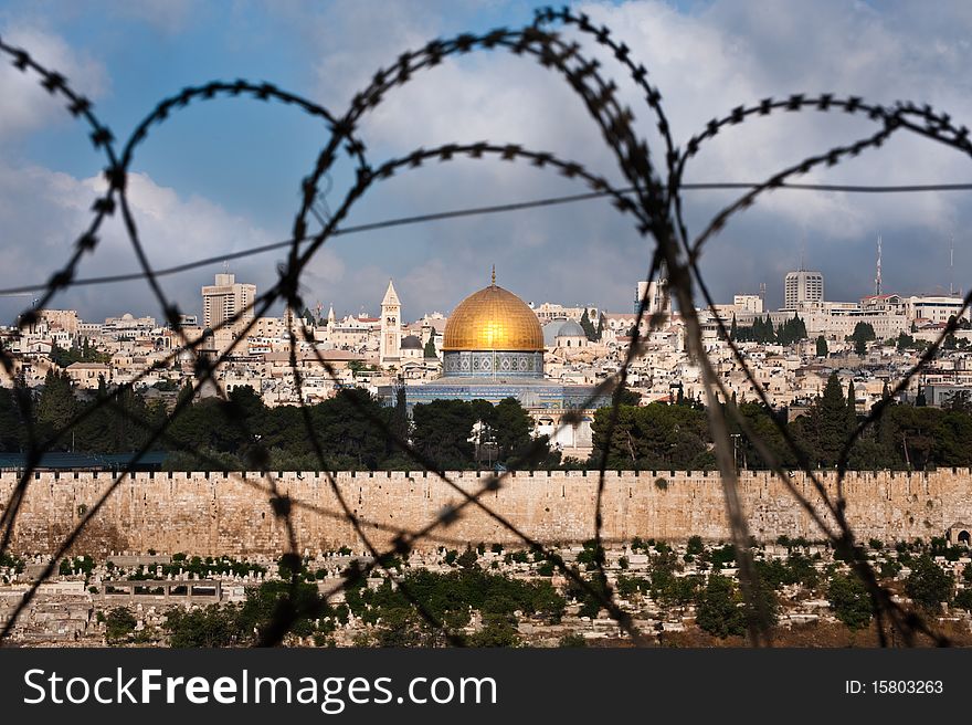 The Old City of Jerusalem, including the Dome of the Rock and various church steeples, seen through coils of razor wire, illustrating the Holy Land's history of division and conflict. The Old City of Jerusalem, including the Dome of the Rock and various church steeples, seen through coils of razor wire, illustrating the Holy Land's history of division and conflict.