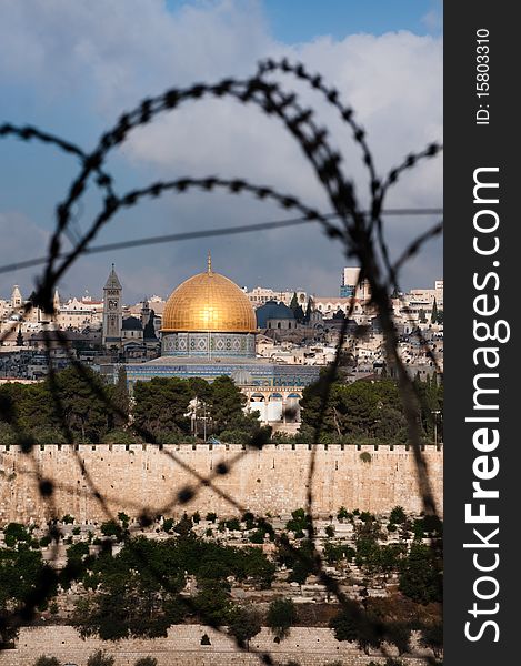 The Old City of Jerusalem, including the Dome of the Rock and various church steeples, seen through coils of razor wire, illustrating the Holy Land's history of division and conflict. The Old City of Jerusalem, including the Dome of the Rock and various church steeples, seen through coils of razor wire, illustrating the Holy Land's history of division and conflict.