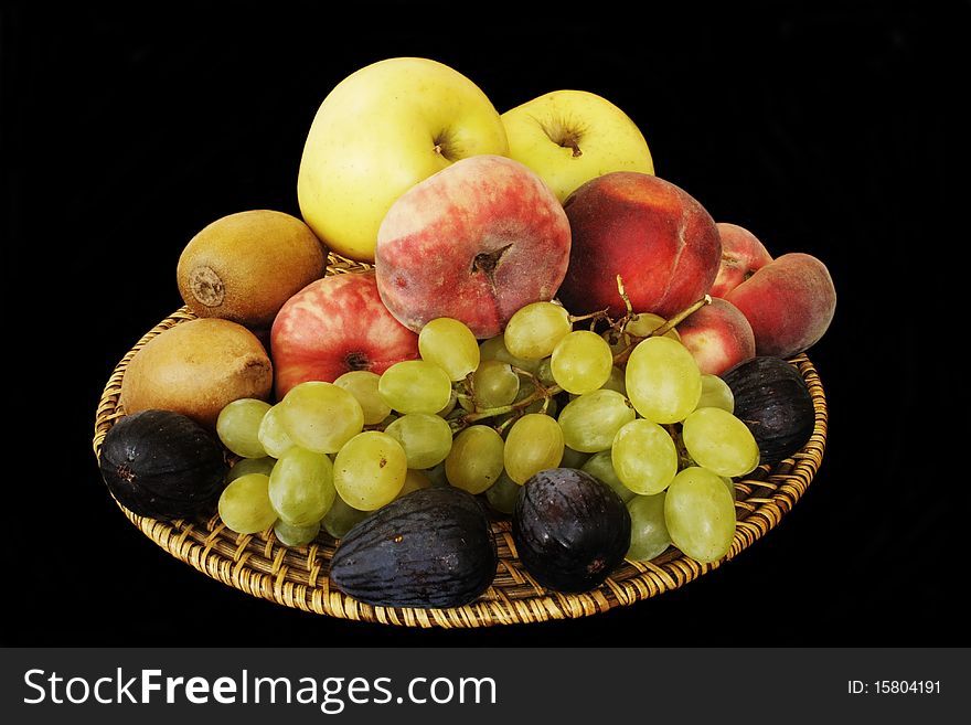 Wicker wooden plate with various fruits in isolated over black. Wicker wooden plate with various fruits in isolated over black