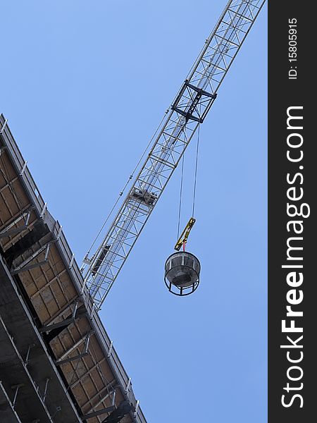 Crane transporting equipment at highrise development, against bright blue sky. Crane transporting equipment at highrise development, against bright blue sky