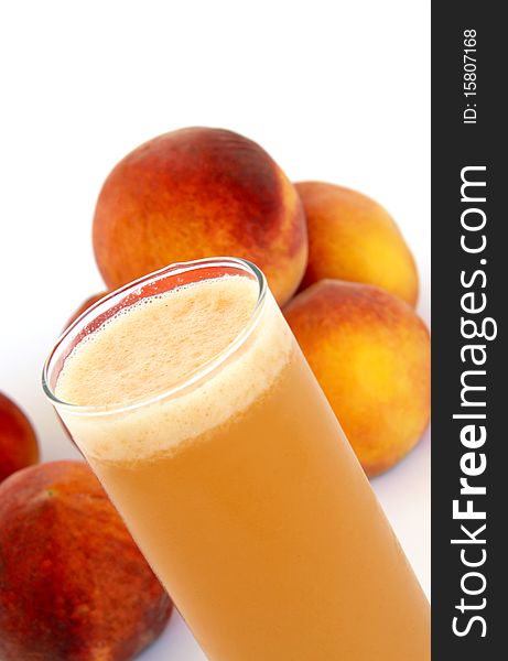 A glass of peach juice in front of peaches isolated on white background. A glass of peach juice in front of peaches isolated on white background.