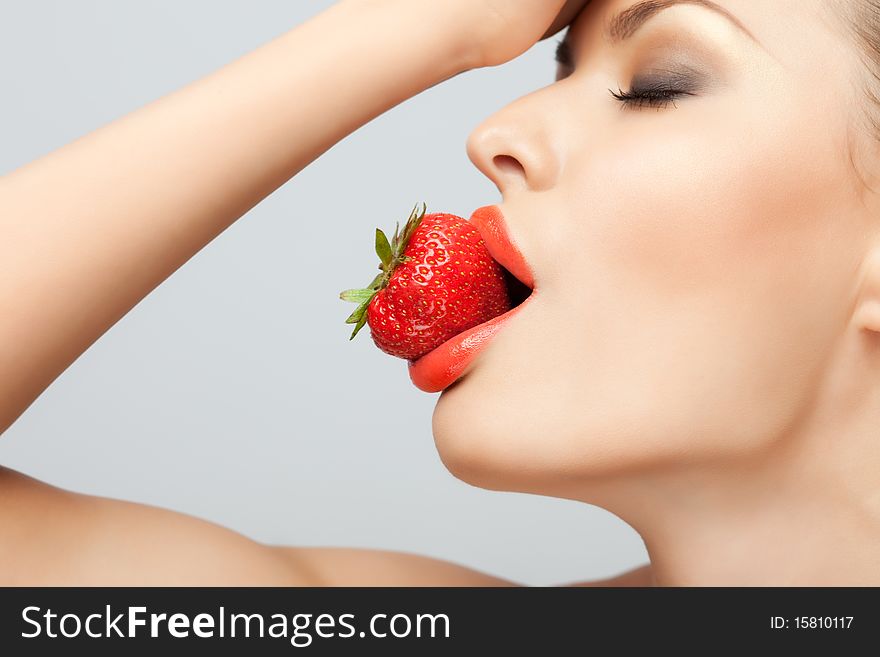 A portrait of a nude woman holding a red-ripe strawberry in her mouth. A portrait of a nude woman holding a red-ripe strawberry in her mouth.