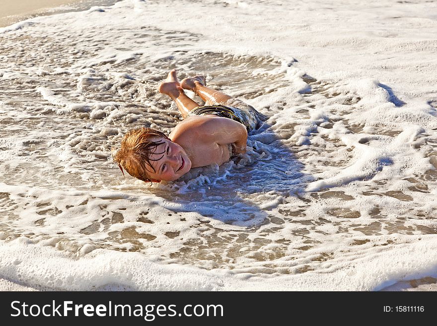 Young boy lying at the beach and playing in the spume. Young boy lying at the beach and playing in the spume