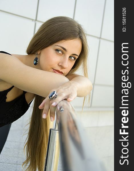 Portrait of elegantly beautiful young woman is based on the railing. The girl beautiful jewelry, ring and earrings with large blue stones. Portrait of elegantly beautiful young woman is based on the railing. The girl beautiful jewelry, ring and earrings with large blue stones