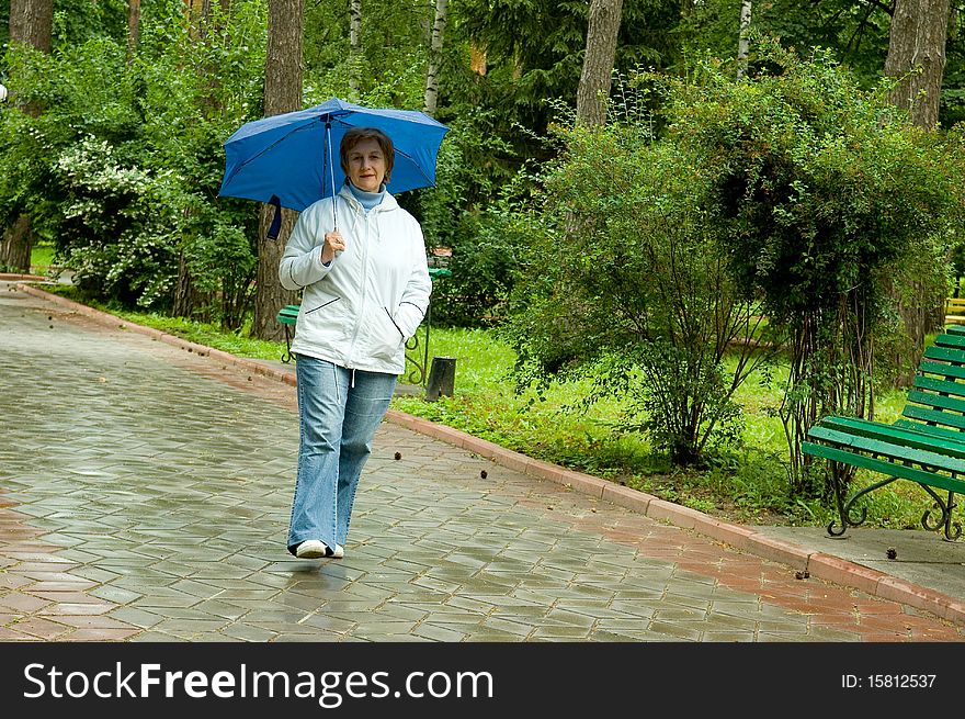 Elderly woman walks in park under rain with umbrella
