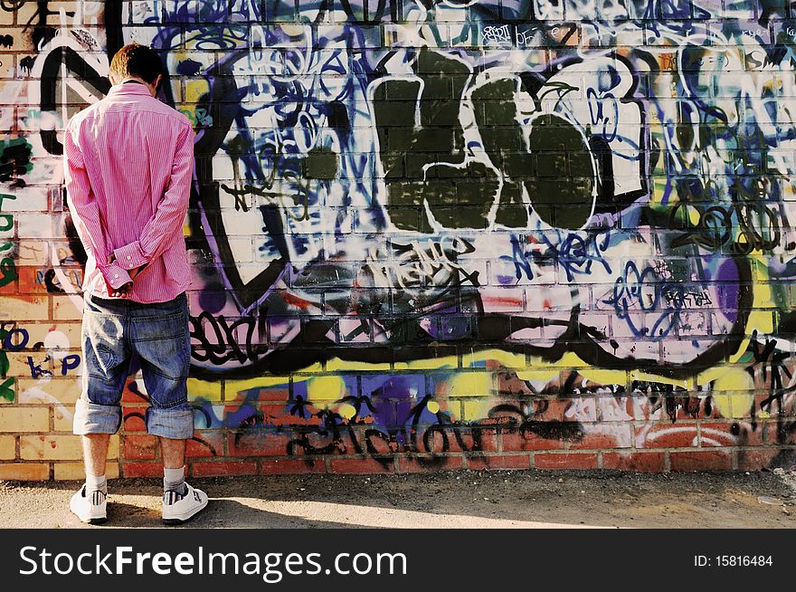 Young Teenager facing his back the camera, wearing a striped shirt and jean shorts against Graffiti Wall.No recognizable inscriptions on the wall. Young Teenager facing his back the camera, wearing a striped shirt and jean shorts against Graffiti Wall.No recognizable inscriptions on the wall.