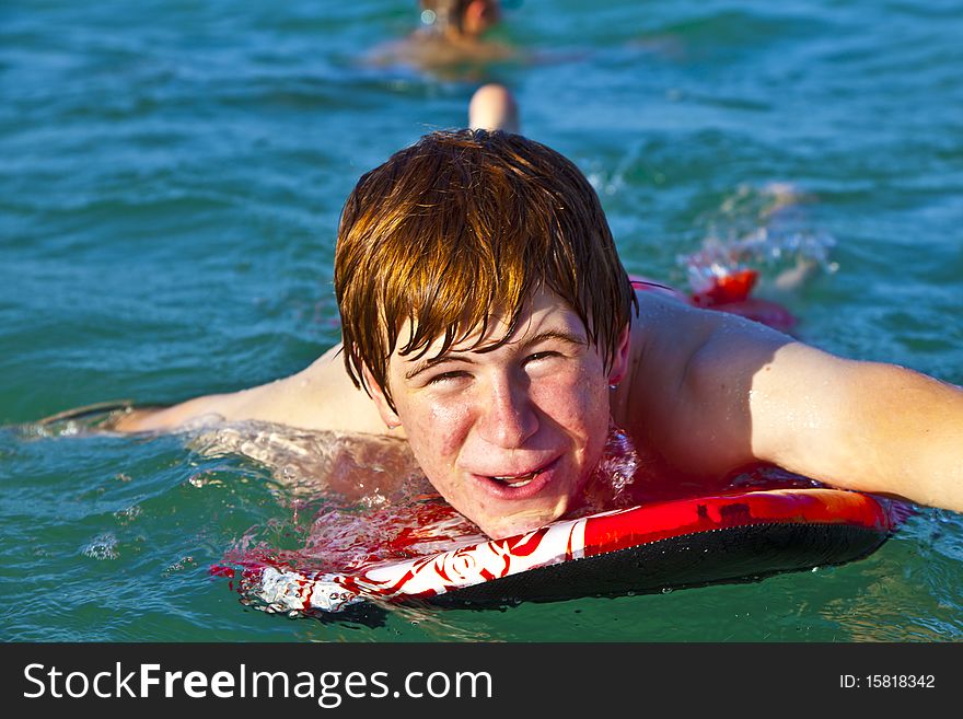Young boy is crawling on the surfboard in the ocean