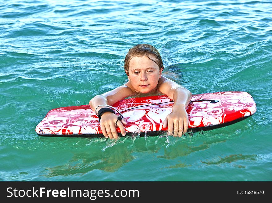 Boy is crawling on the surfboard in the ocean