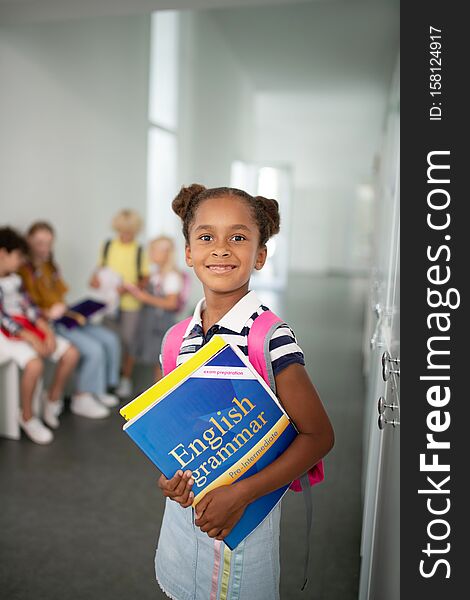 Girl with books. Cute dark-skinned girl wearing striped t-shirt holding books while standing at school. Girl with books. Cute dark-skinned girl wearing striped t-shirt holding books while standing at school