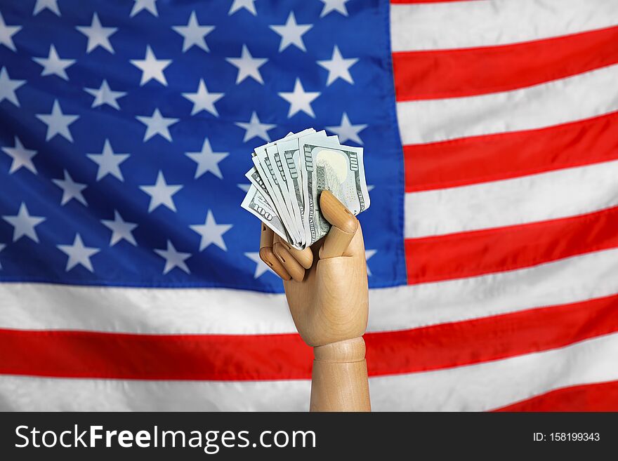 Wooden mannequin hand with fan of banknotes against USA national flag