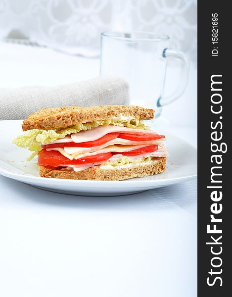 Fresh and delicious classic club sandwich over a white glass dish with glass cup