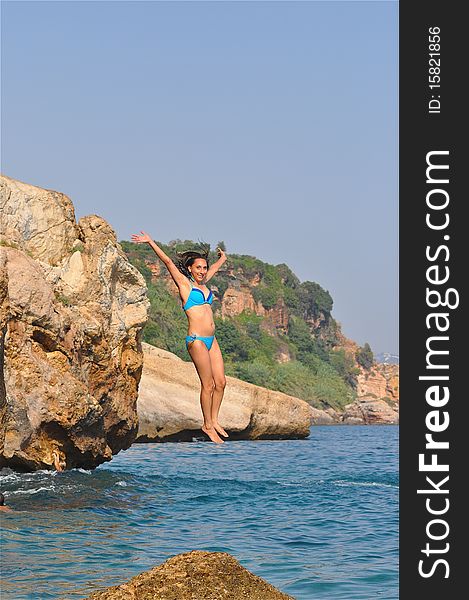 A young woman is jumping from a huge rock to the ocean. A young woman is jumping from a huge rock to the ocean