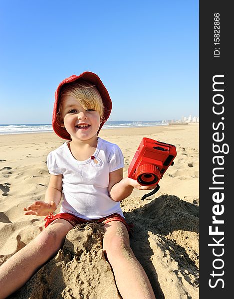 Adorable little girl takes pictures with her red camera on the beach. Adorable little girl takes pictures with her red camera on the beach