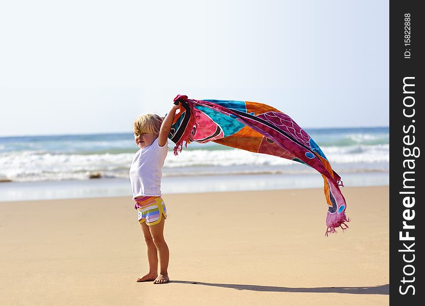 Young cute blonde child on vacation is holding a sarong in the wind. Young cute blonde child on vacation is holding a sarong in the wind