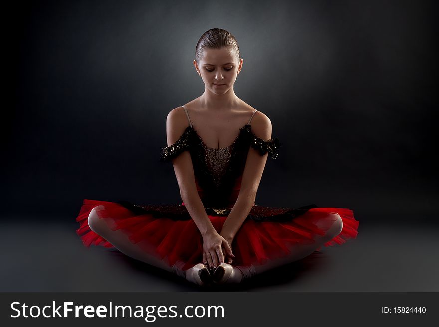 Picture of a beautiful ballerina sitting on a dark background