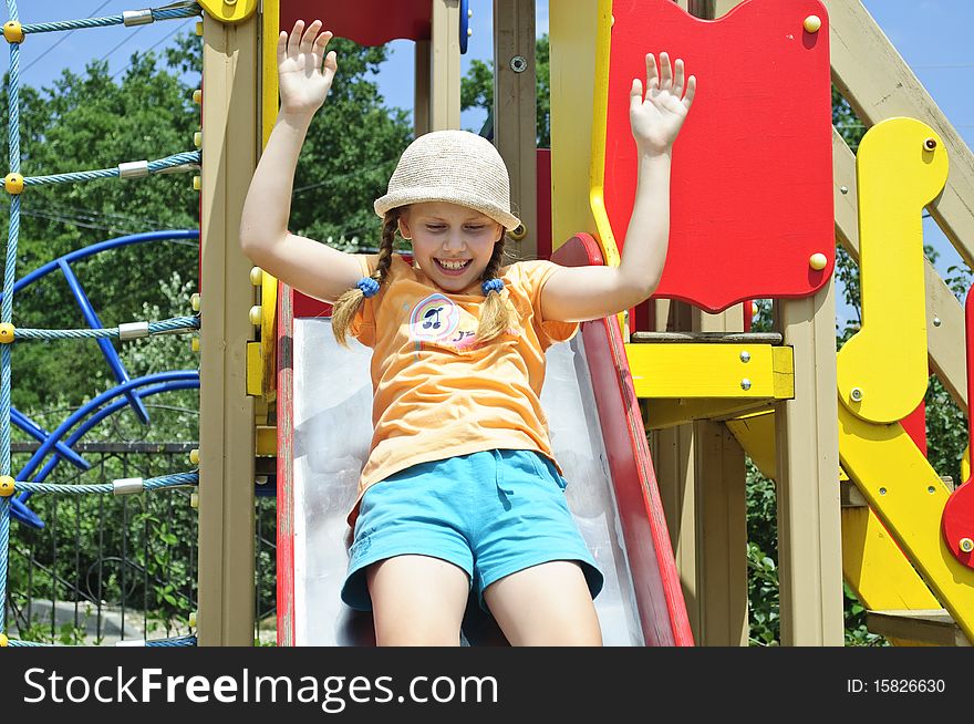 A girl in a hat with plaits plays on a playground. A girl in a hat with plaits plays on a playground