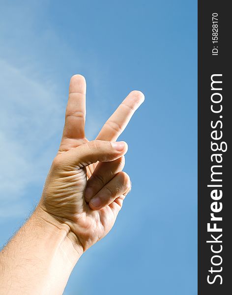 Photo of one hand, which shows the V, against the blue sky. Photo of one hand, which shows the V, against the blue sky